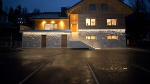 A modern two-story house with a stone facade, wooden exterior, and a driveway leading to a garage. - Vila Alpina (Bled)