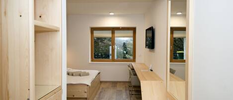 Un dormitorio pequeño con una cama, un escritorio y una ventana con vistas a árboles.