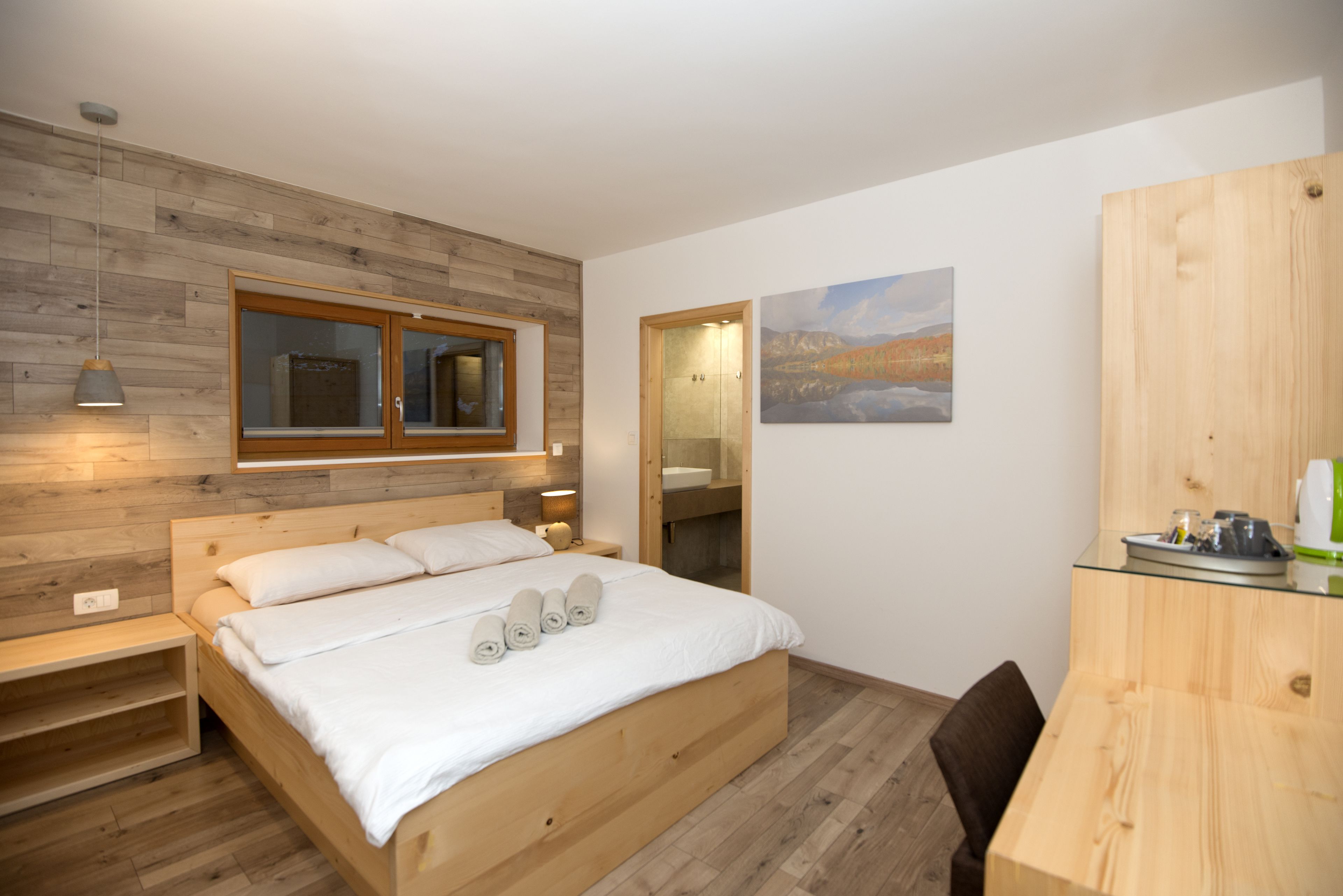 A modern bedroom with a wooden bed, a bedside table, a nightstand, a mirror, and a small desk with a chair.