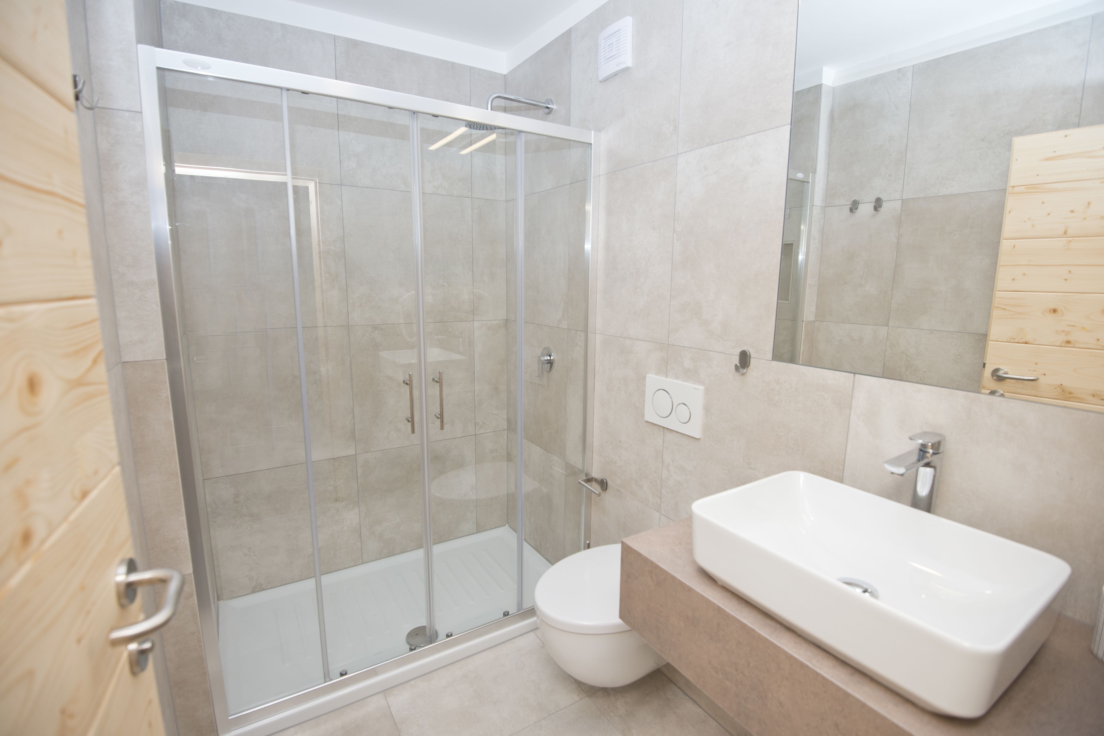 A modern bathroom with a glass-enclosed shower, a white sink, and a wooden vanity.