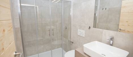 Un baño moderno con ducha de vidrio, lavamanos blanco y tocador de madera.