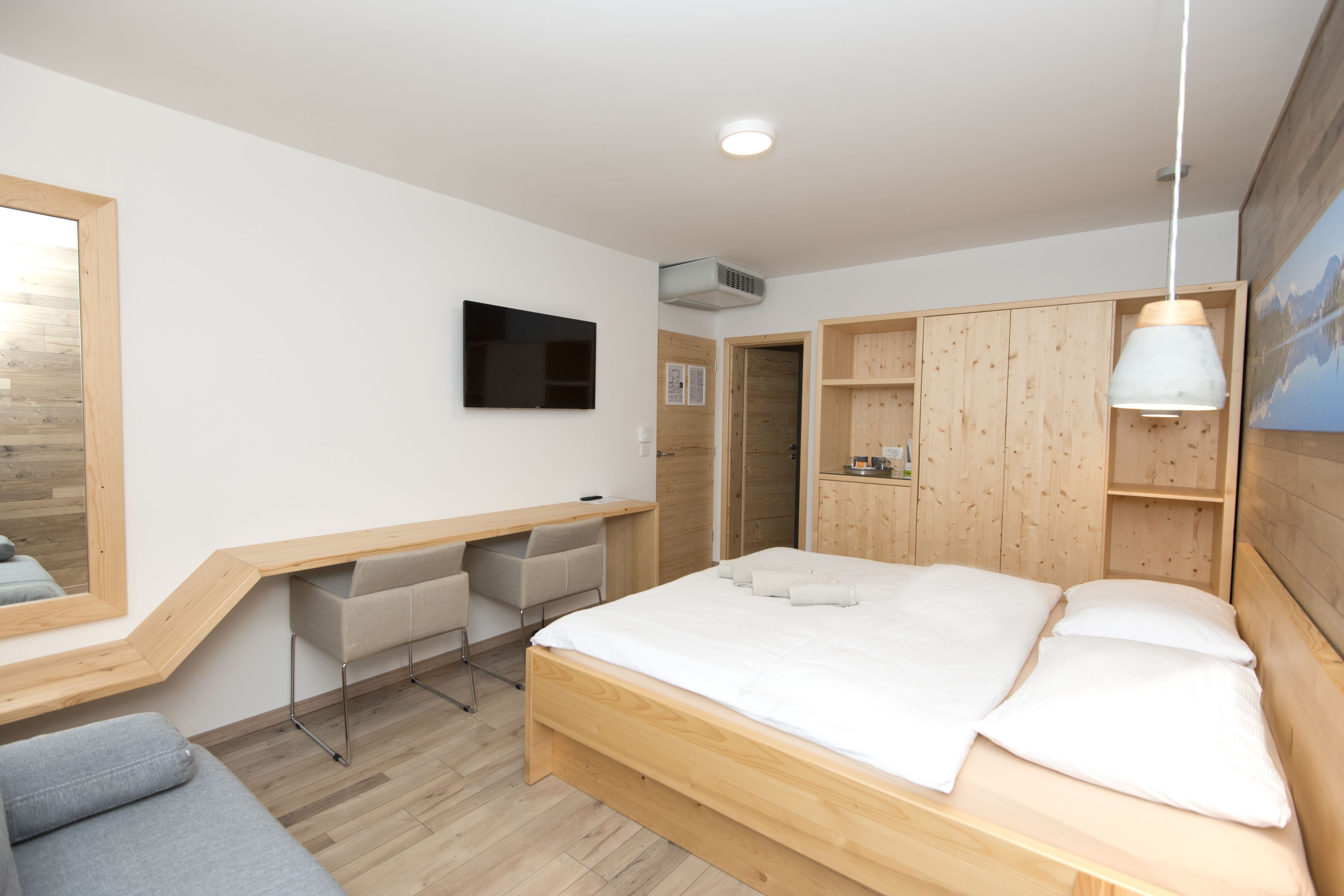 A modern bedroom with a wooden bed, a desk, and a TV mounted on the wall.