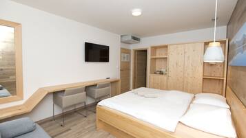 A modern bedroom with a wooden bed, a desk, and a TV mounted on the wall.