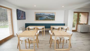 Un coin repas avec une table et des chaises en bois, un banc vert et deux tableaux accrochés aux murs.