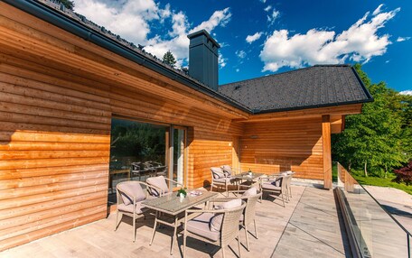 A wooden cabin with a patio area featuring wicker furniture and a glass door leading to a deck.