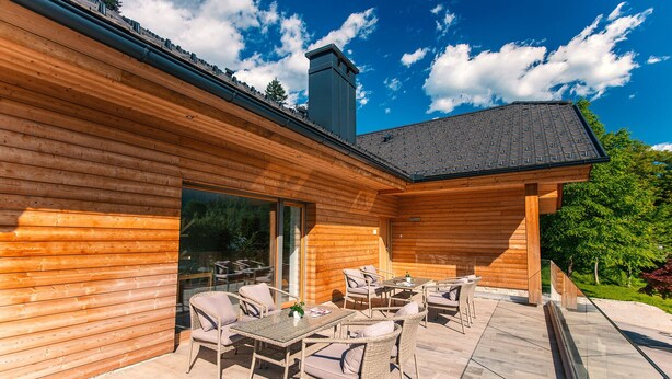 A wooden cabin with a patio area featuring wicker furniture and a glass door leading to a deck. - Vila Alpina (Bled)