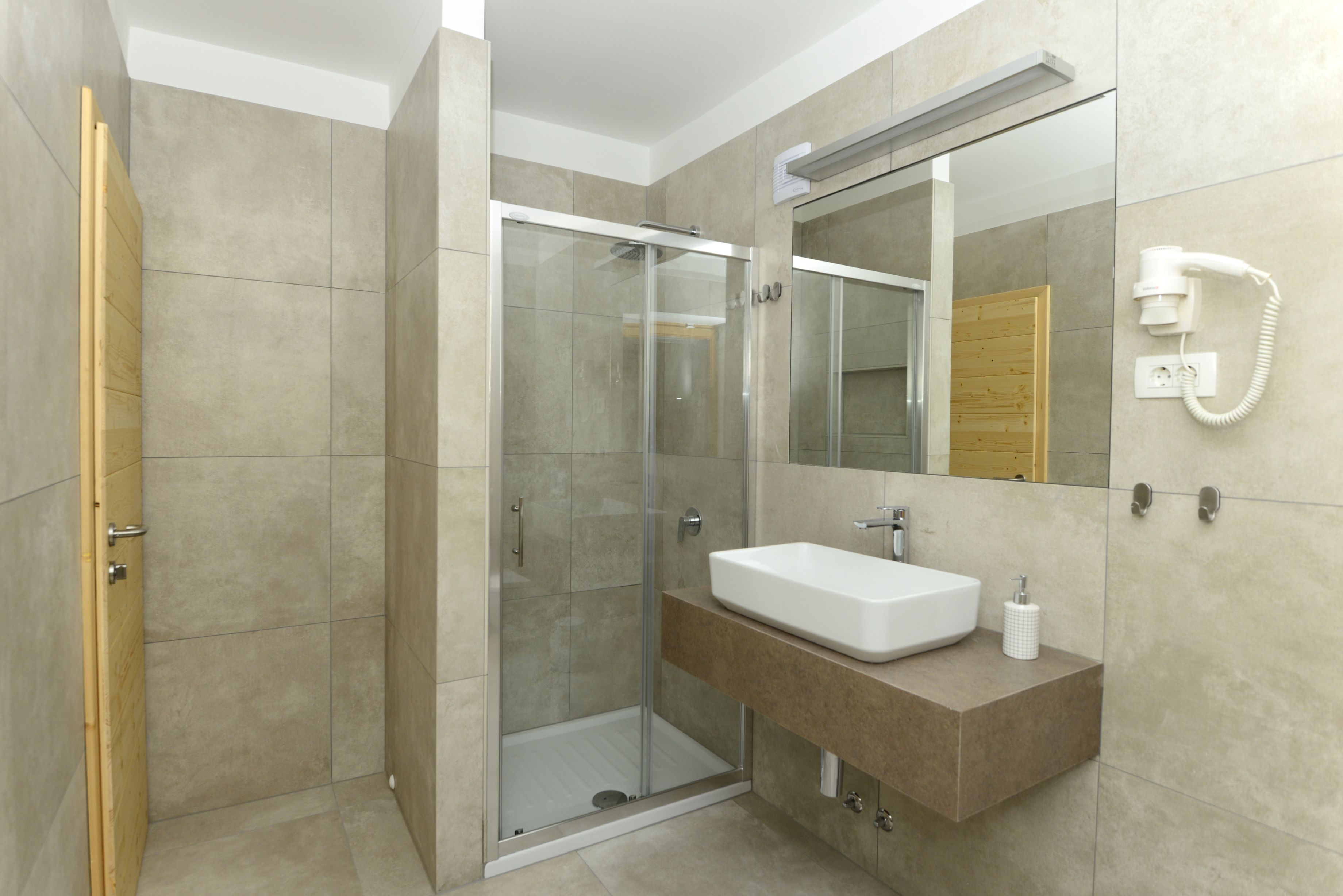 A modern bathroom with a glass-enclosed shower, a white sink, and a mirror with a built-in phone.