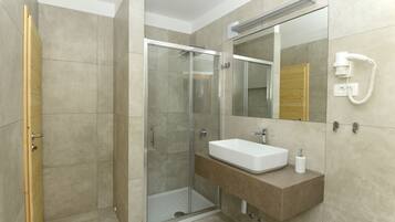 A modern bathroom with a glass-enclosed shower, a white sink, and a mirror with a built-in phone.