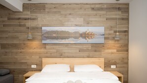 A neatly made bed with white linens and rolled towels, a wooden headboard, and a large framed picture of a lake and mountains on the wall. - Vila Alpina (Bled)