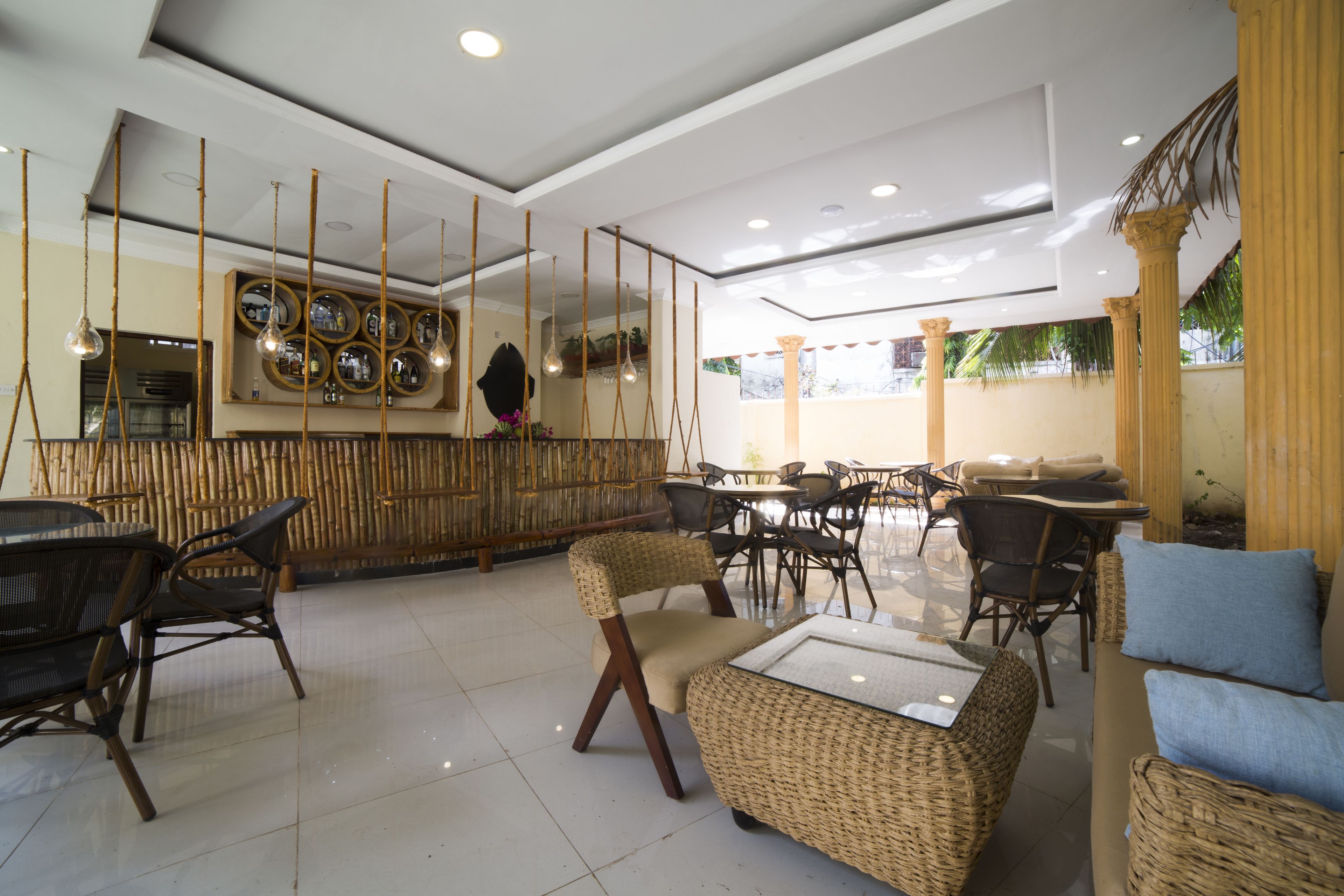 A spacious indoor area with wicker furniture, a bar area with mirrors, and a ceiling with hanging lights.