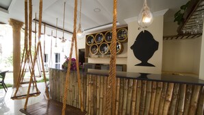 Un espace d’accueil décoré sur le thème du bambou, comprenant un comptoir, des balançoires suspendues en corde et un mur orné de miroirs ronds.