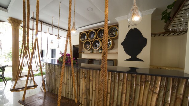 Un espace d’accueil décoré sur le thème du bambou, comprenant un comptoir, des balançoires suspendues en corde et un mur orné de miroirs ronds.