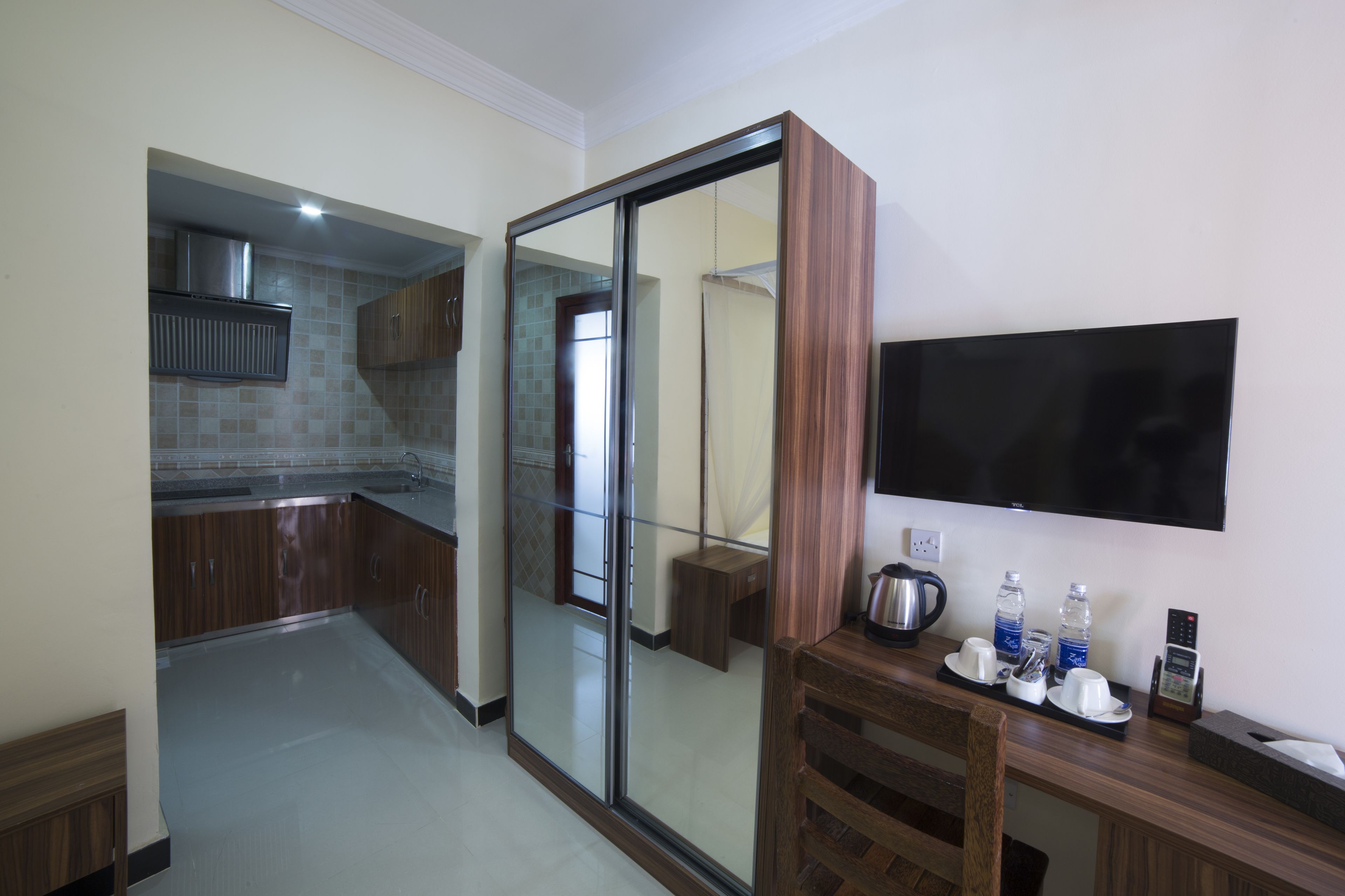 Una cocina moderna con una puerta corrediza de vidrio que da al baño, un televisor de pantalla plana en la pared y una mesita con una tetera, tazas y una botella de agua.