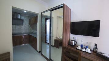 Una cocina moderna con una puerta corrediza de vidrio que da al baño, un televisor de pantalla plana en la pared y una mesita con una tetera, tazas y una botella de agua.