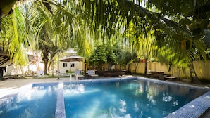 Une piscine dont les bords sont recouverts de carreaux, entourée de palmiers et agrémentée de mobilier d’extérieur.
