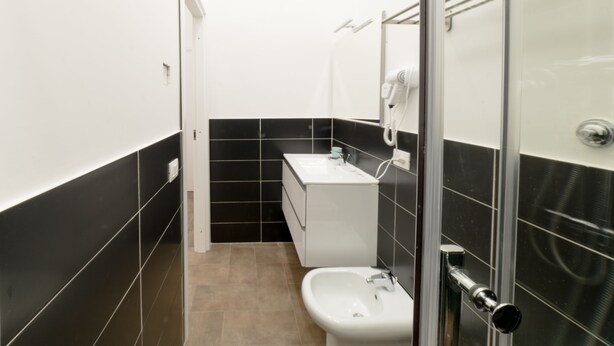 A modern bathroom with a white sink, a mirror, and a glass shower enclosure. - Boutique Toledo (Naples)