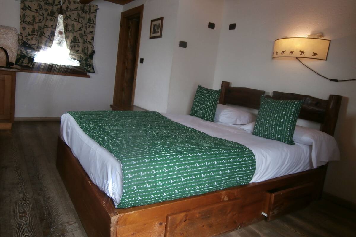 A wooden bed with a green patterned bedspread and white pillows in a room with a wooden ceiling and a wall-mounted light fixture.