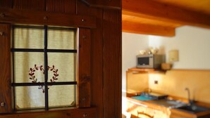 A wooden-framed window with a decorative wreath, a kitchen with wooden cabinets, a microwave, and a sink. - Baita Ancienne Bergerie (Valtournenche)