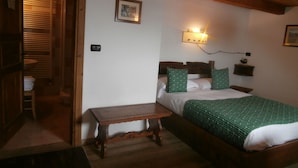 A bedroom with a wooden bed, a bedside table, a wall-mounted light, and a small shelf. - Baita Ancienne Bergerie (Valtournenche)