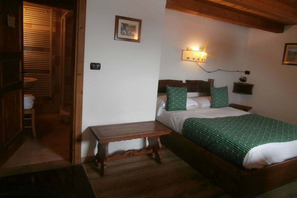A bedroom with a wooden bed, a bedside table, a wall-mounted light, and a small shelf.