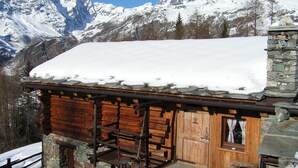A rustic wooden cabin with a snow-covered roof, set against a backdrop of snow-capped mountains. - Baita Ancienne Bergerie (Valtournenche)