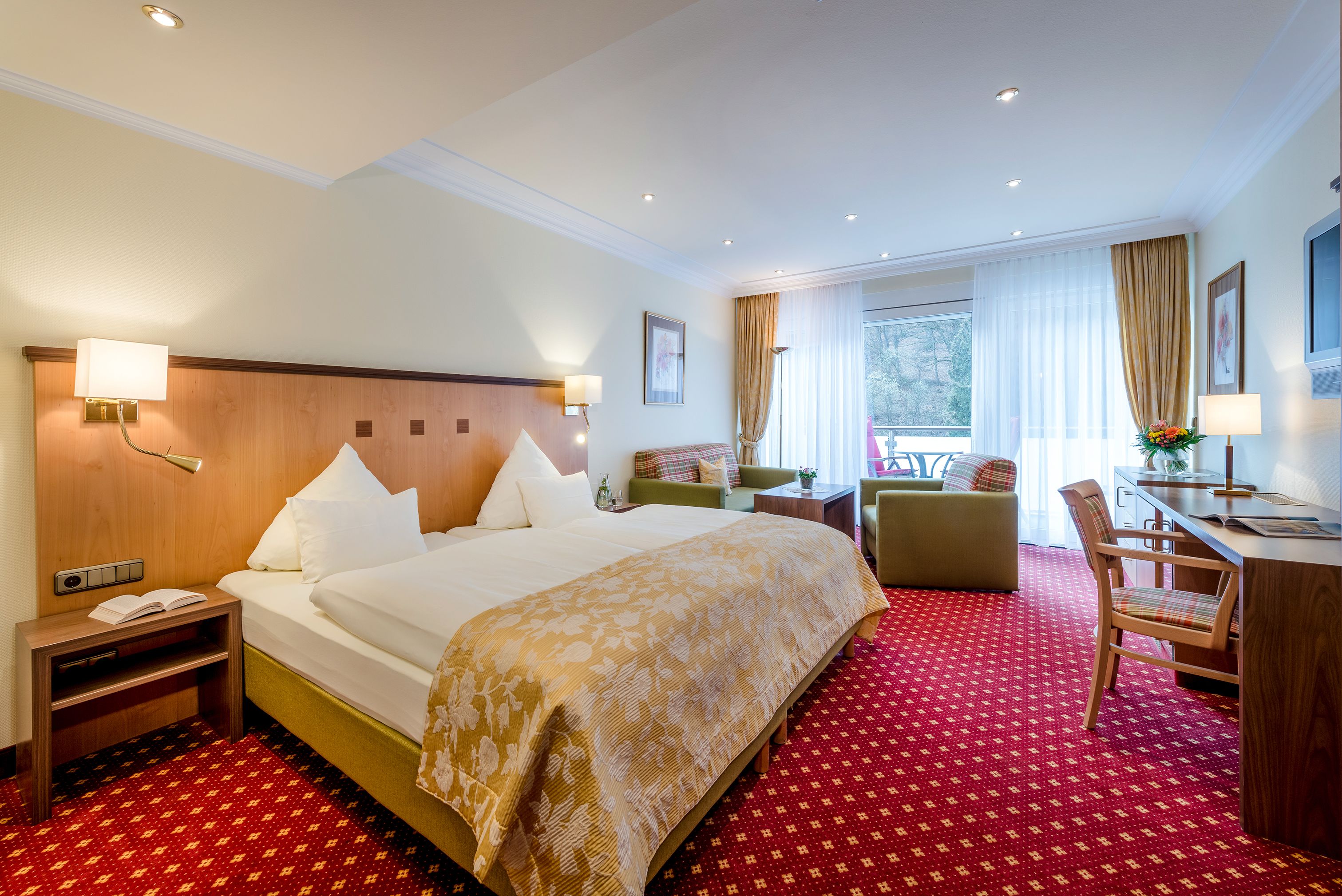 A hotel room with a large bed, a desk, a chair, a small table, and a window with curtains.