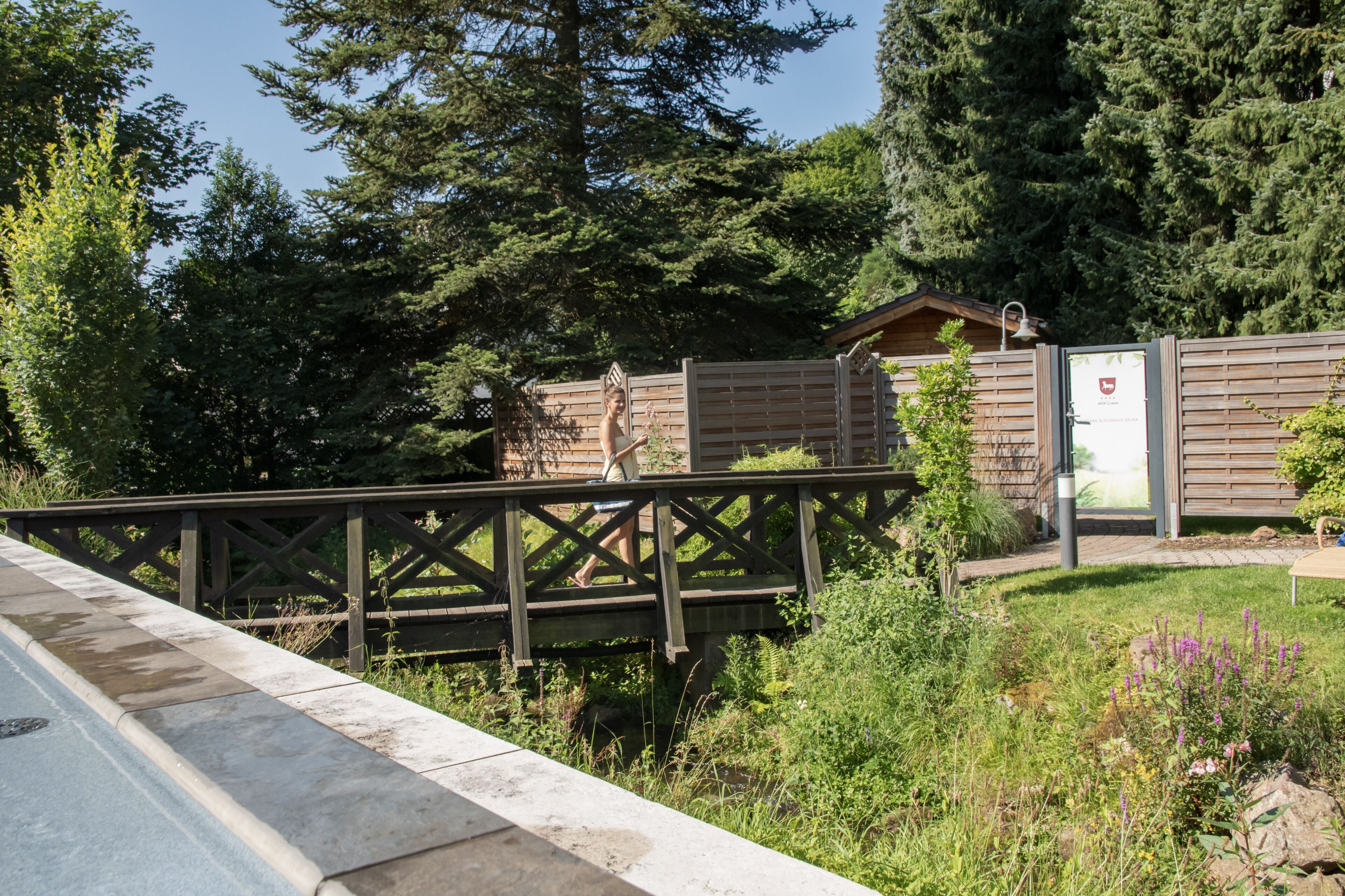 A wooden bridge over a body of water, leading to a cabin with a metal door and a small shed nearby.