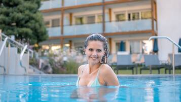 A swimming pool with a person in it, surrounded by a building with multiple floors and balconies.