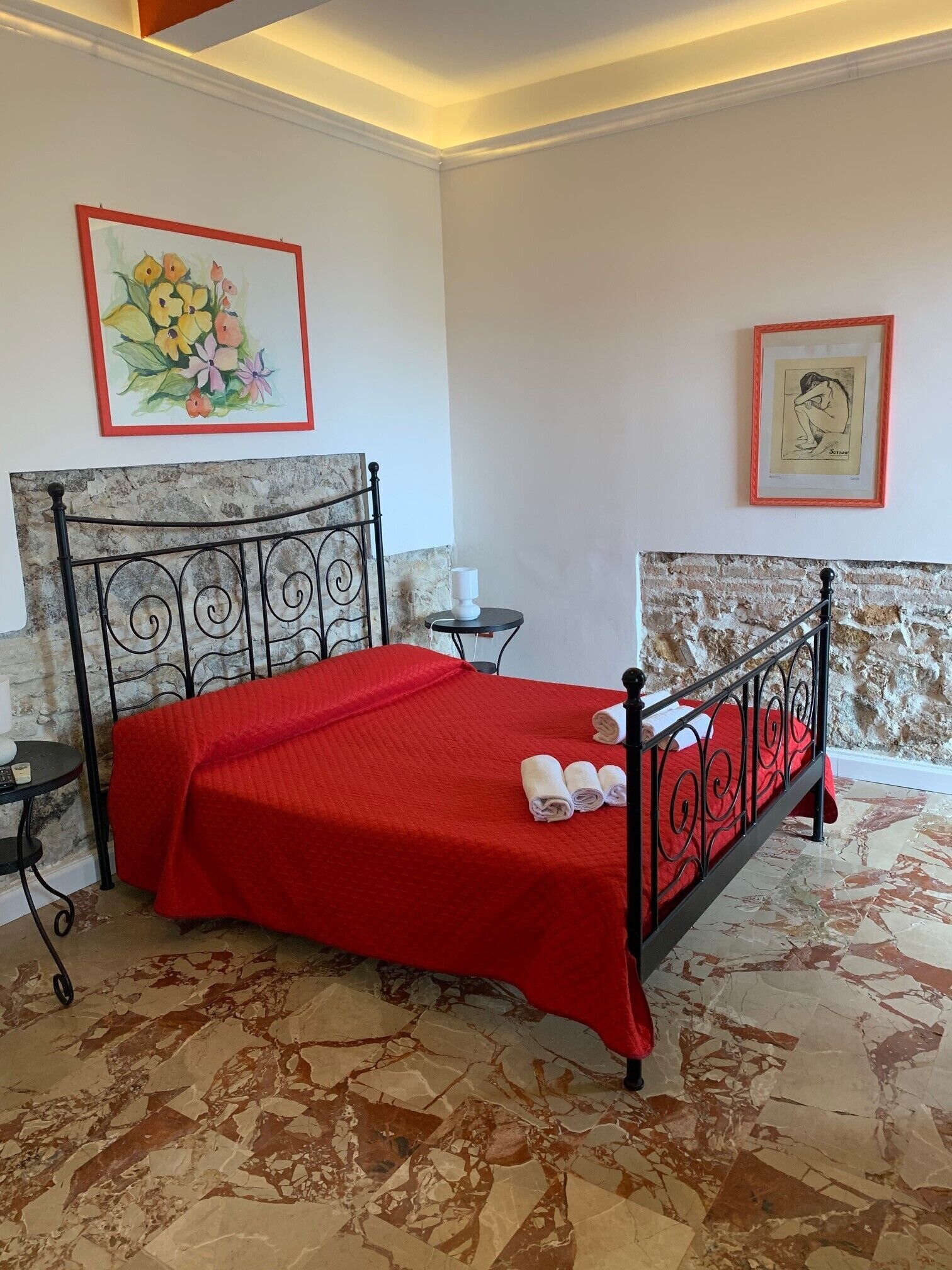 A room with a bed, a small table, and two framed artworks on the walls.