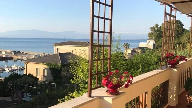 Un balcon avec vue sur la mer et les montagnes, des balustrades en bois et des plantes en pot.