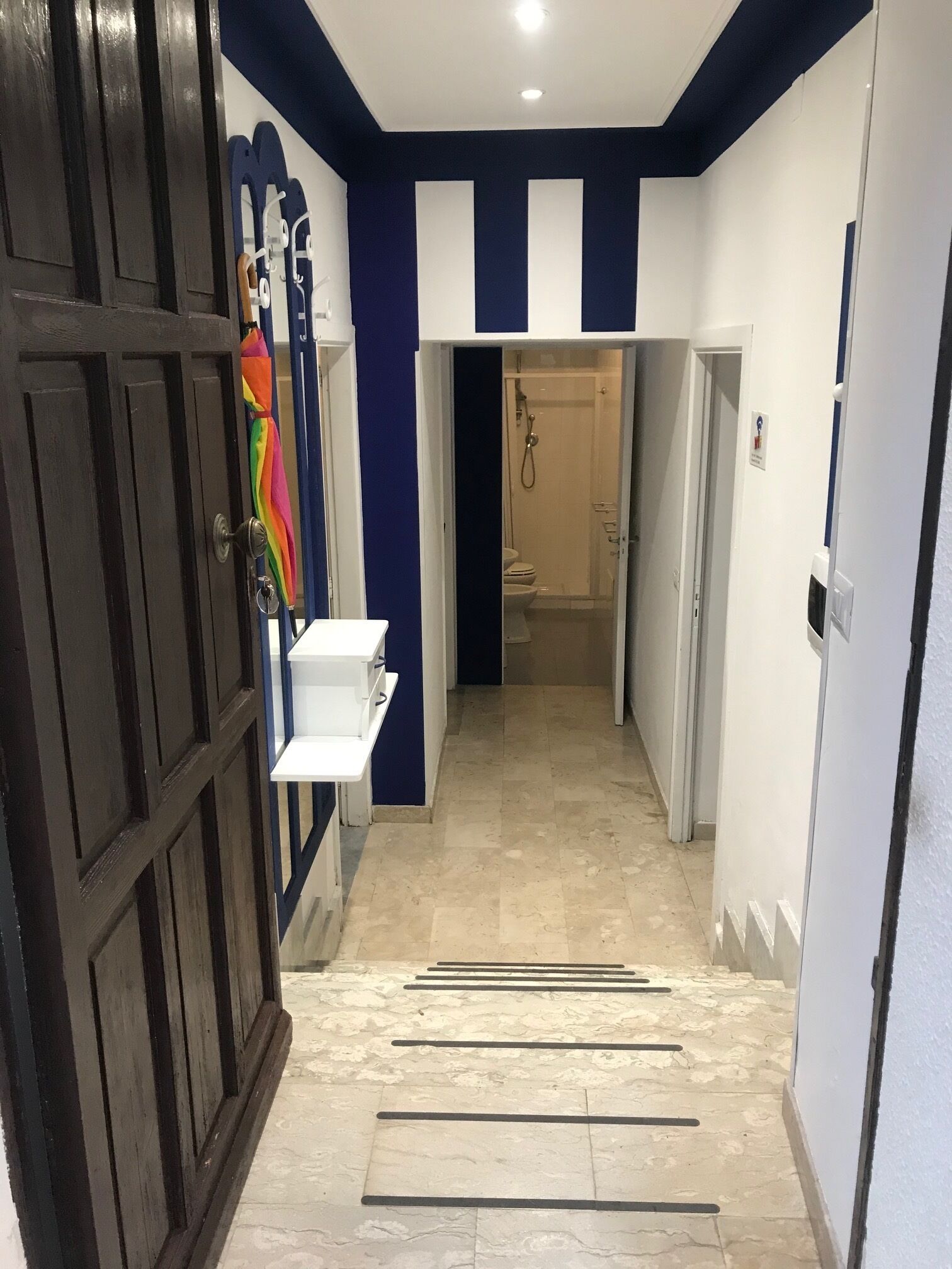 Un couloir avec une porte en bois sombre, une étagère blanche et un sol carrelé.