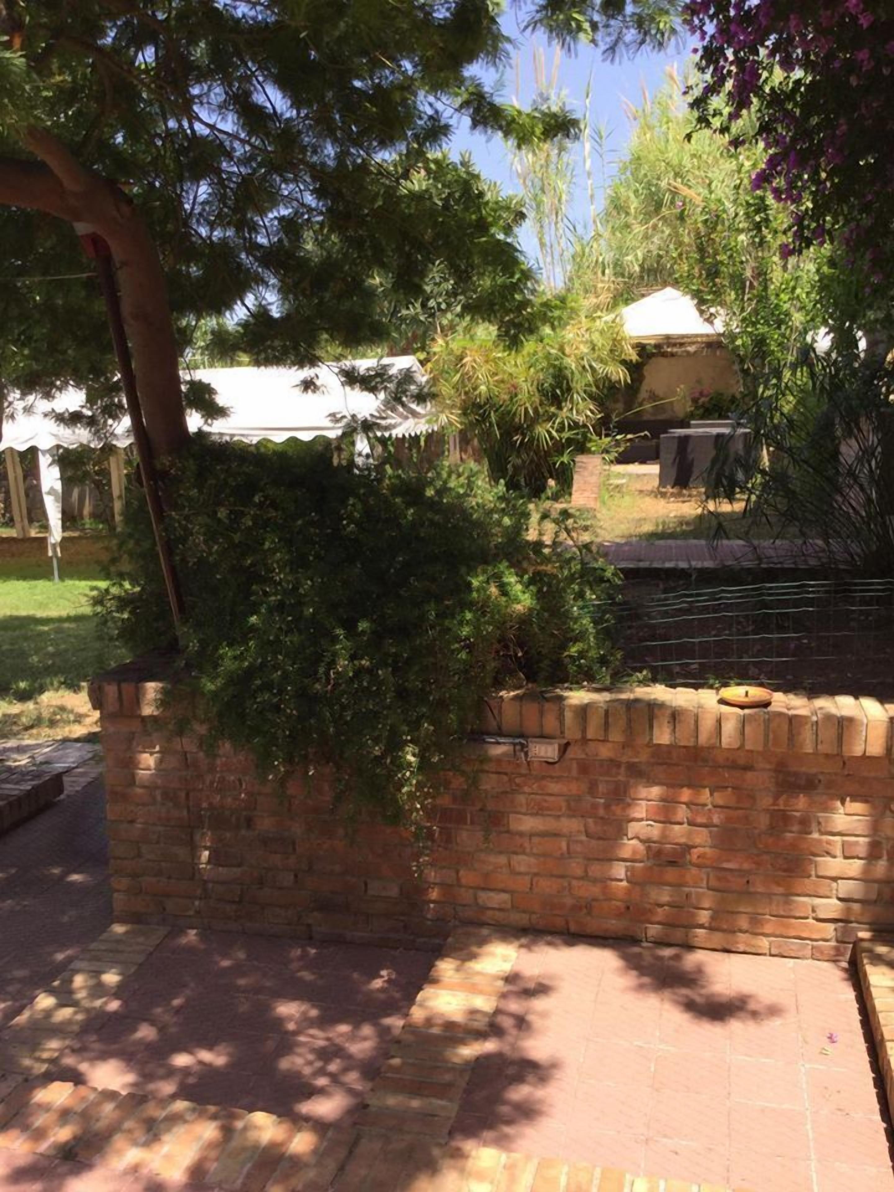 Eine Ziegelmauer mit einem kleinen Gartenbereich, einem Weg und einem weißen Gebäude im Hintergrund.