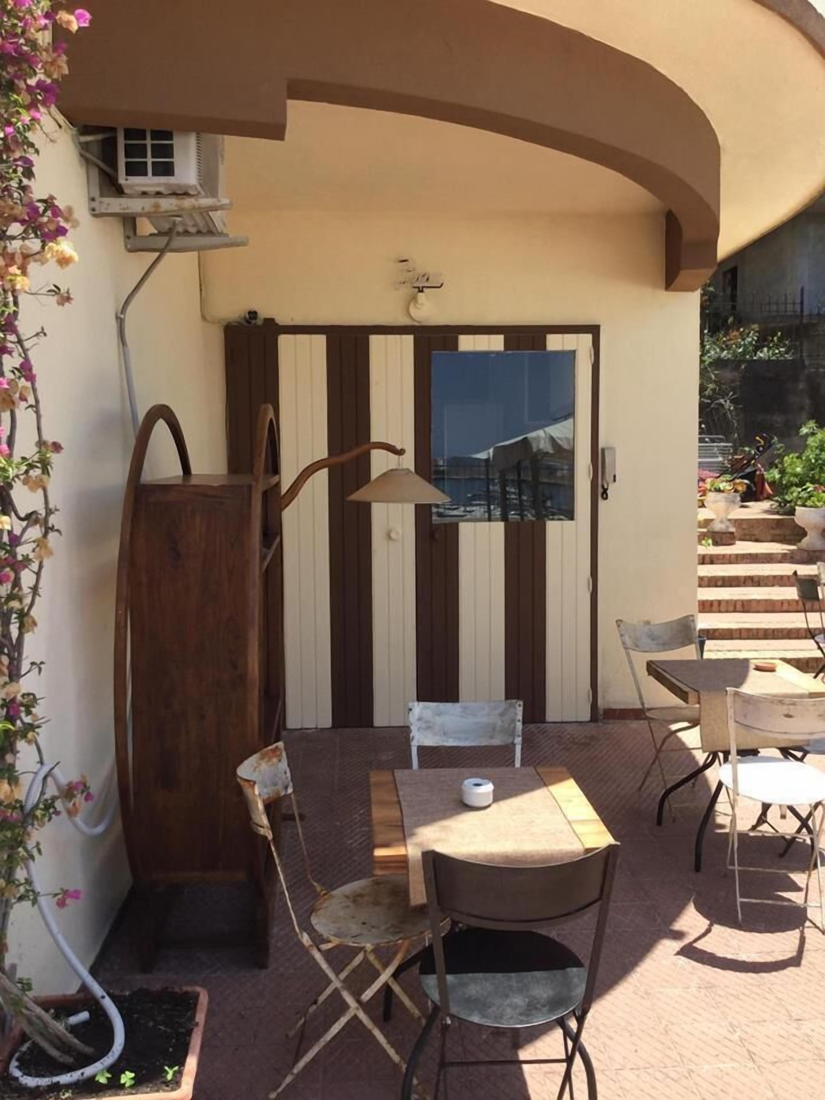 Eine Terrasse mit Tisch und Stühlen, einer Hängelampe und Blick auf ein Gebäude durch ein Fenster.