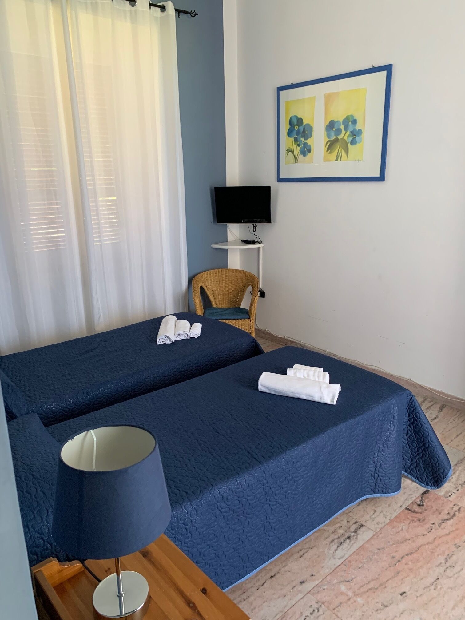 A hotel room with two beds, a TV, a chair, and a painting on the wall.