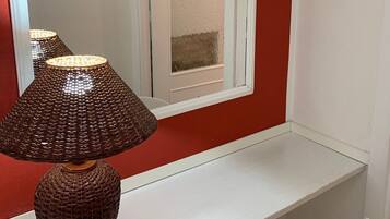 A corner desk with a woven lamp, a white chair, and a red wall.