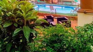 Un espace piscine doté de chaises longues, entouré d’une végétation luxuriante et offrant une vue sur un coucher de soleil se reflétant sur une étendue d’eau.