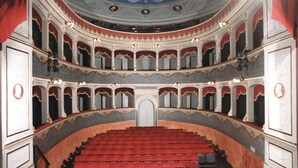 Un teatro majestuoso con varios palcos, techo ricamente decorado y asientos rojos.