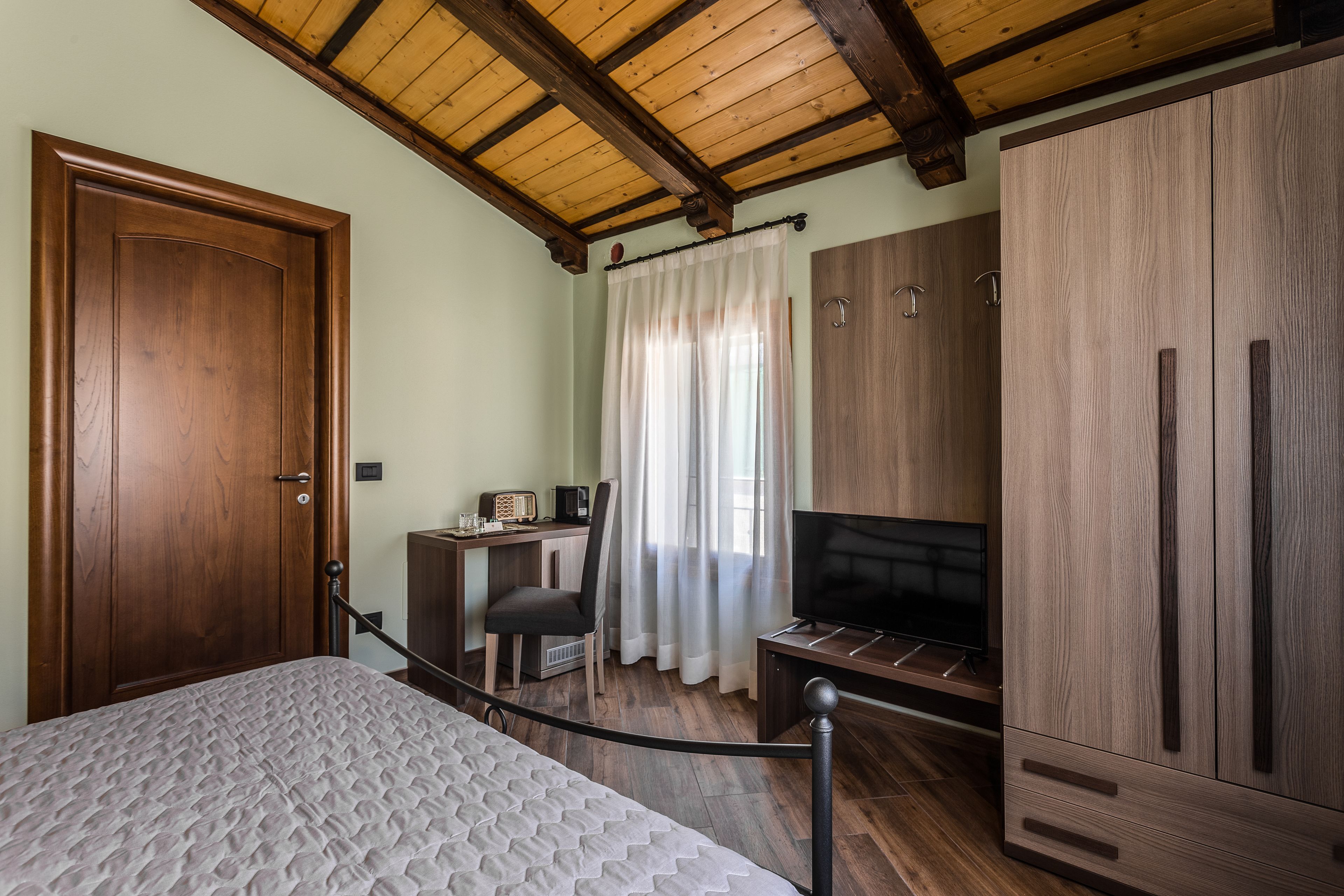 Una camera da letto con una porta in legno, un letto con copripiumino decorato, una scrivania con sedia, una televisione e un armadio.