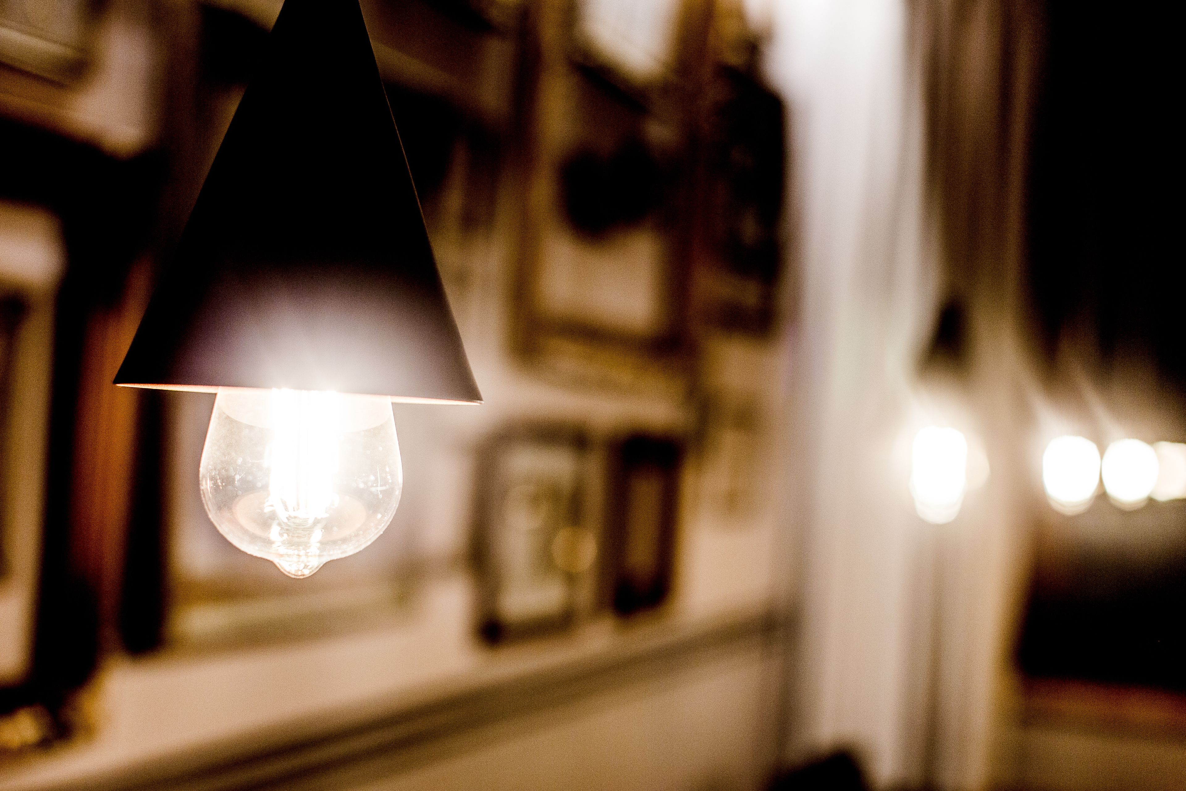 A close-up of a hanging light bulb in a dimly lit room with blurred background details.