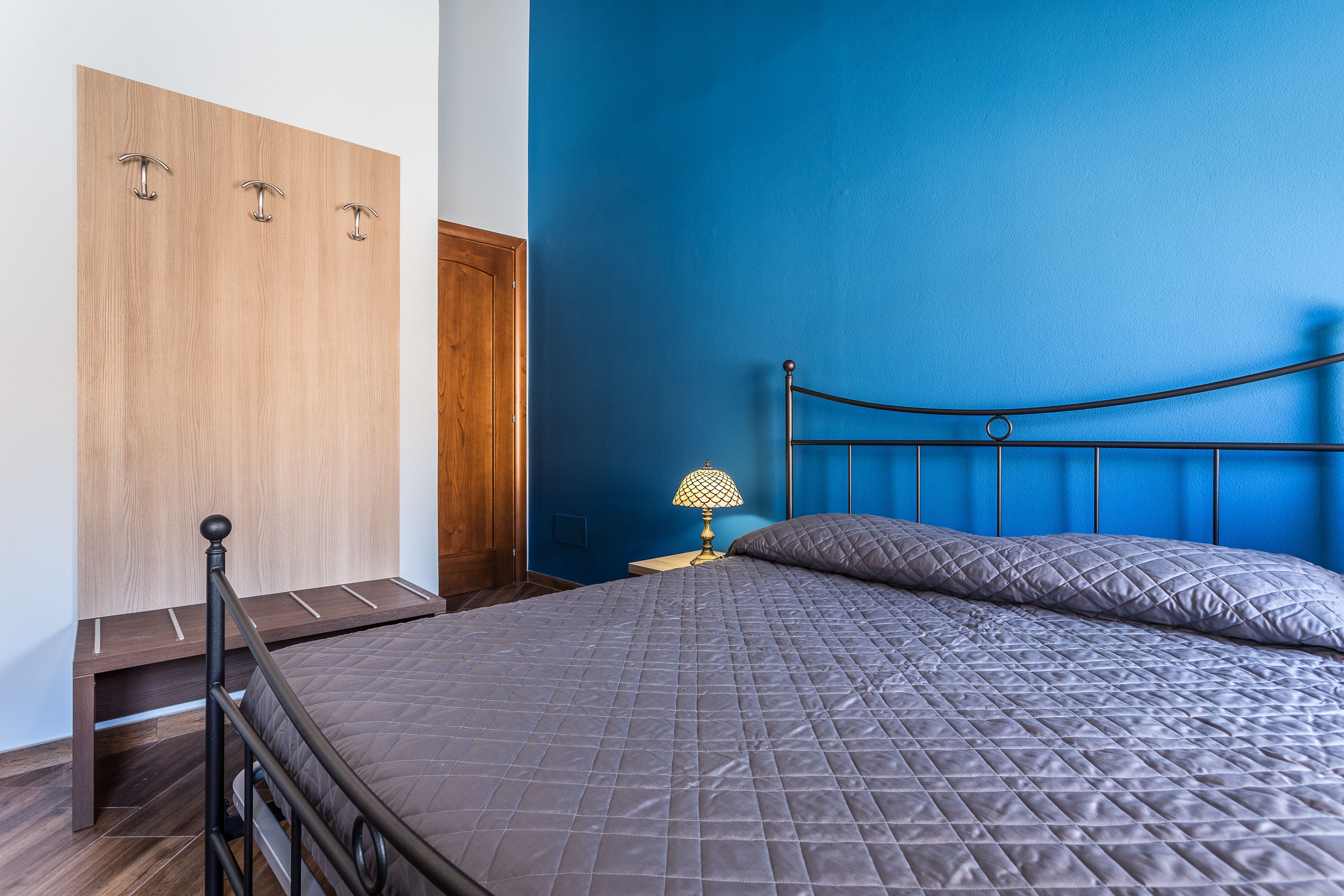 A bedroom with a bed, a nightstand, a lamp, and a wardrobe.