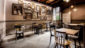 Interior de un restaurante con mesas y sillas de madera, cuadros enmarcados en la pared y lámparas colgantes.