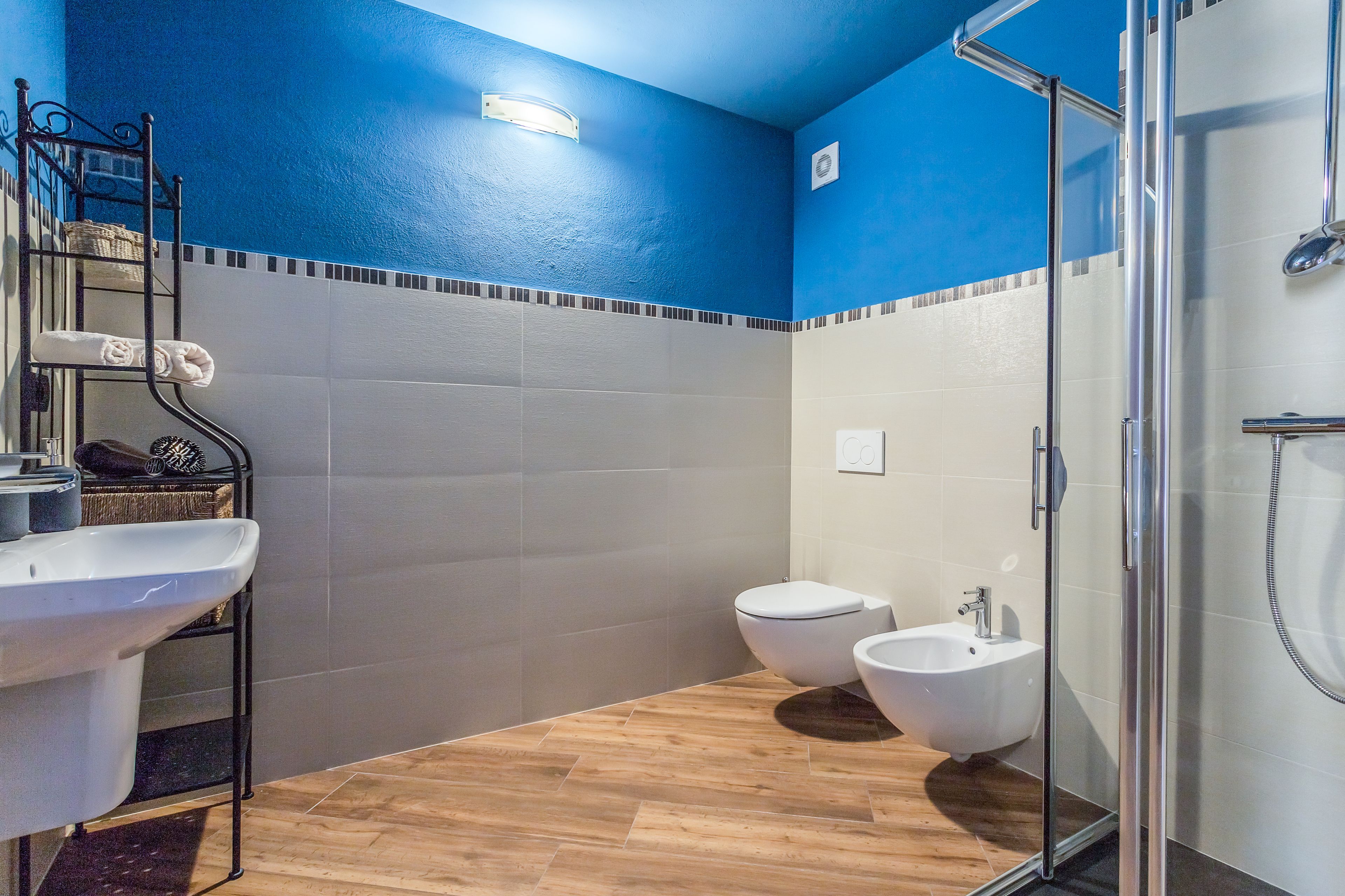 A modern bathroom with a wooden floor, a bidet, a toilet, and a glass shower enclosure.