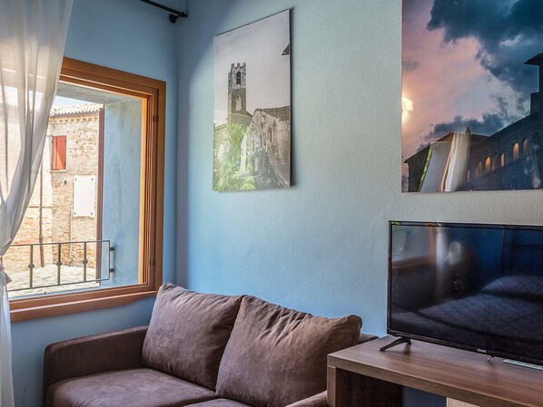 Una habitación con ventana, un sofá, un televisor y dos cuadros en la pared.