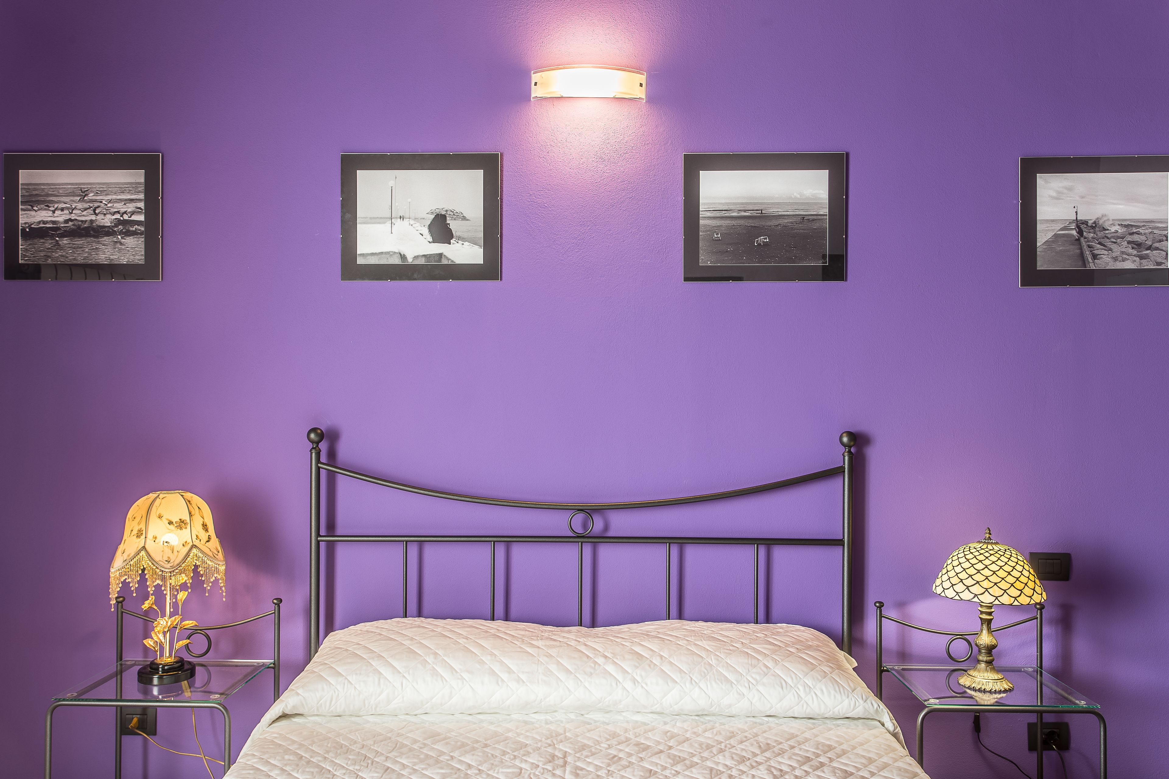 Un dormitorio con una cama, dos mesitas de noche con lámparas, y tres cuadros en la pared.
