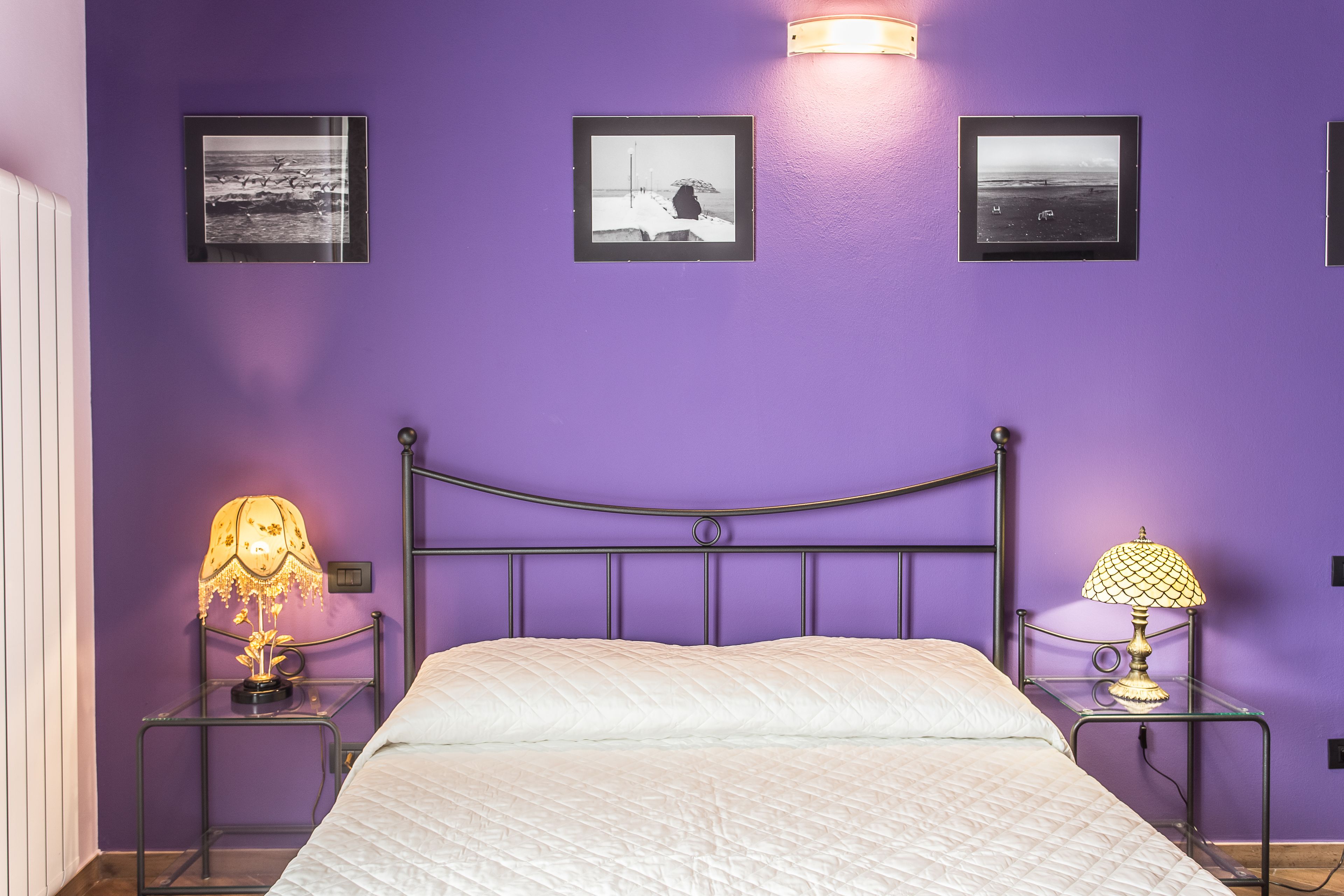 A room with a purple wall, a bed with white bedding, and two bedside tables with lamps.