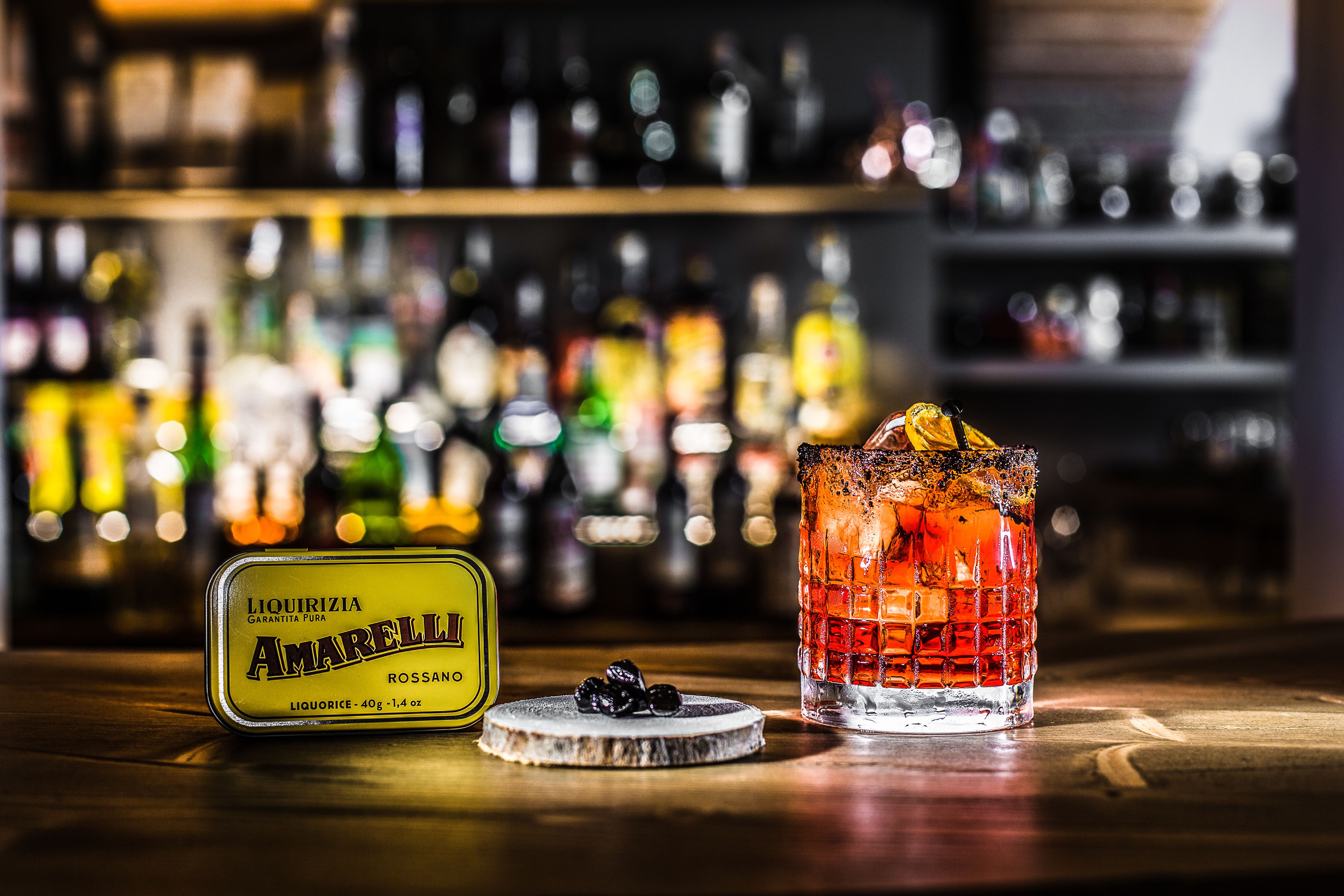 Eine Bar mit einer Flasche Amarella Likör, einem Glas mit Eiswürfeln und einem Untersetzer mit ein paar Oliven.