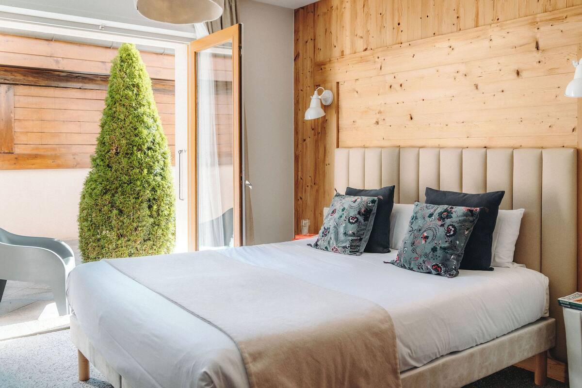 Une chambre avec un grand lit, une tête de lit en bois et un arbre en pot.