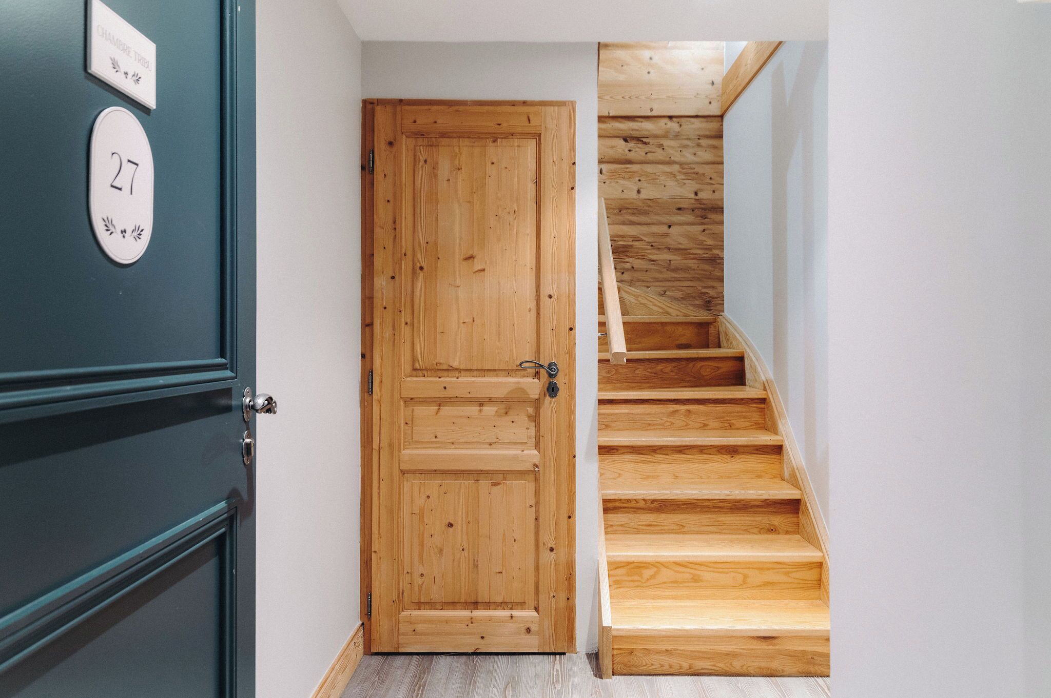 A wooden door with a number plate, a staircase with wooden steps, and a wall with a nameplate.