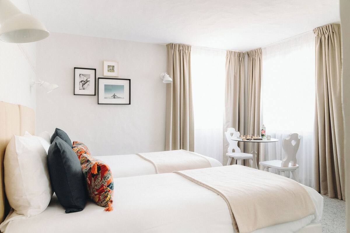 Une chambre d’hôtel avec deux lits, une petite table et une chaise, ainsi que des rideaux.