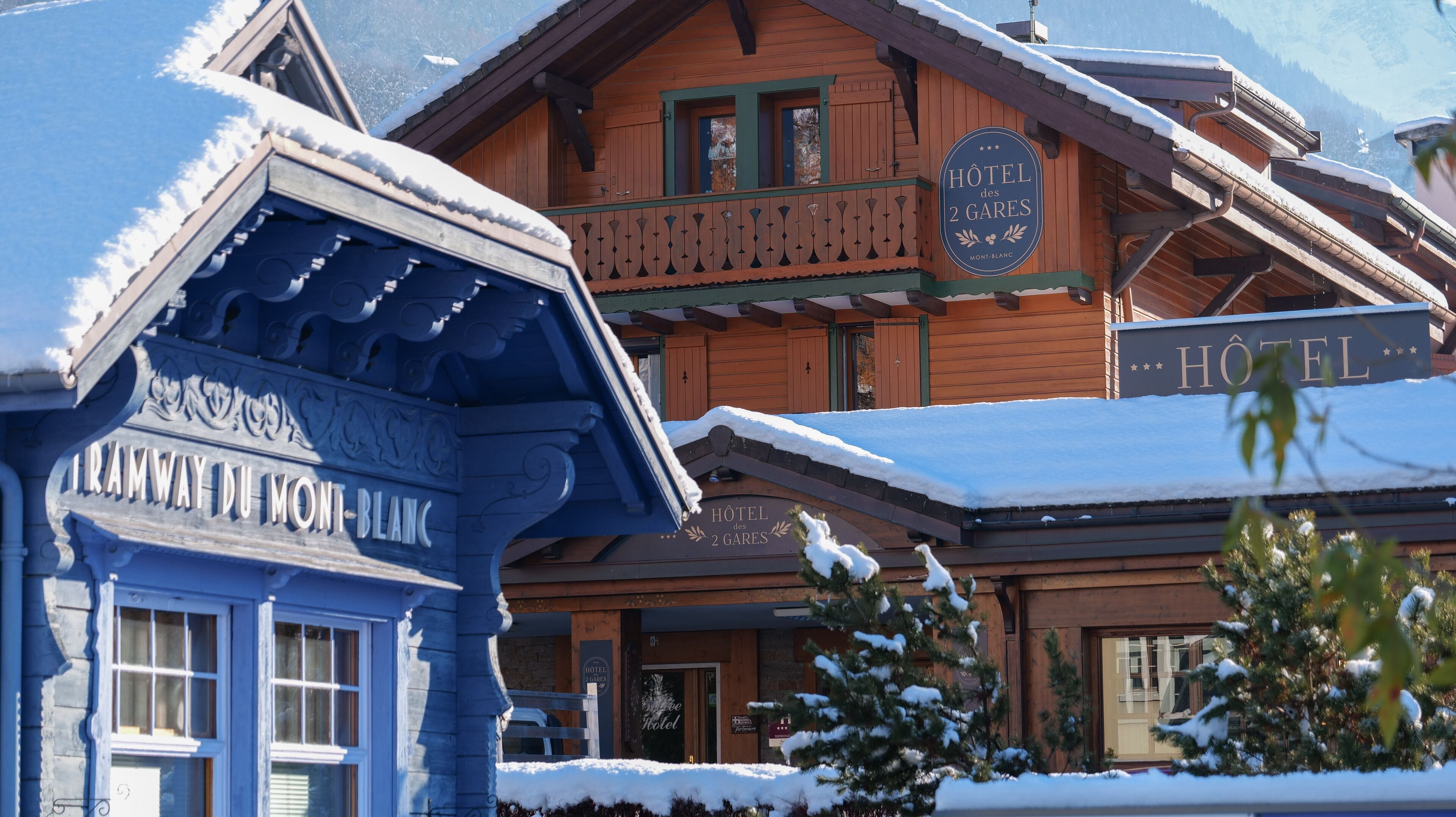 Een houten gebouw met een bord waarop 'Hôtel des 2 Gares' en 'Tramway du Mont-Blanc' staat.